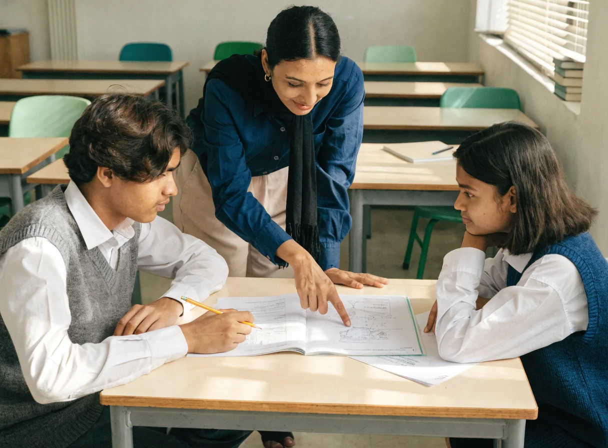 A teacher helping two students with a problem at a desk
