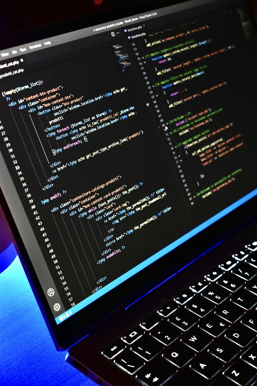 A laptop late at night with a code editor open, coloured syntax across a dark screen