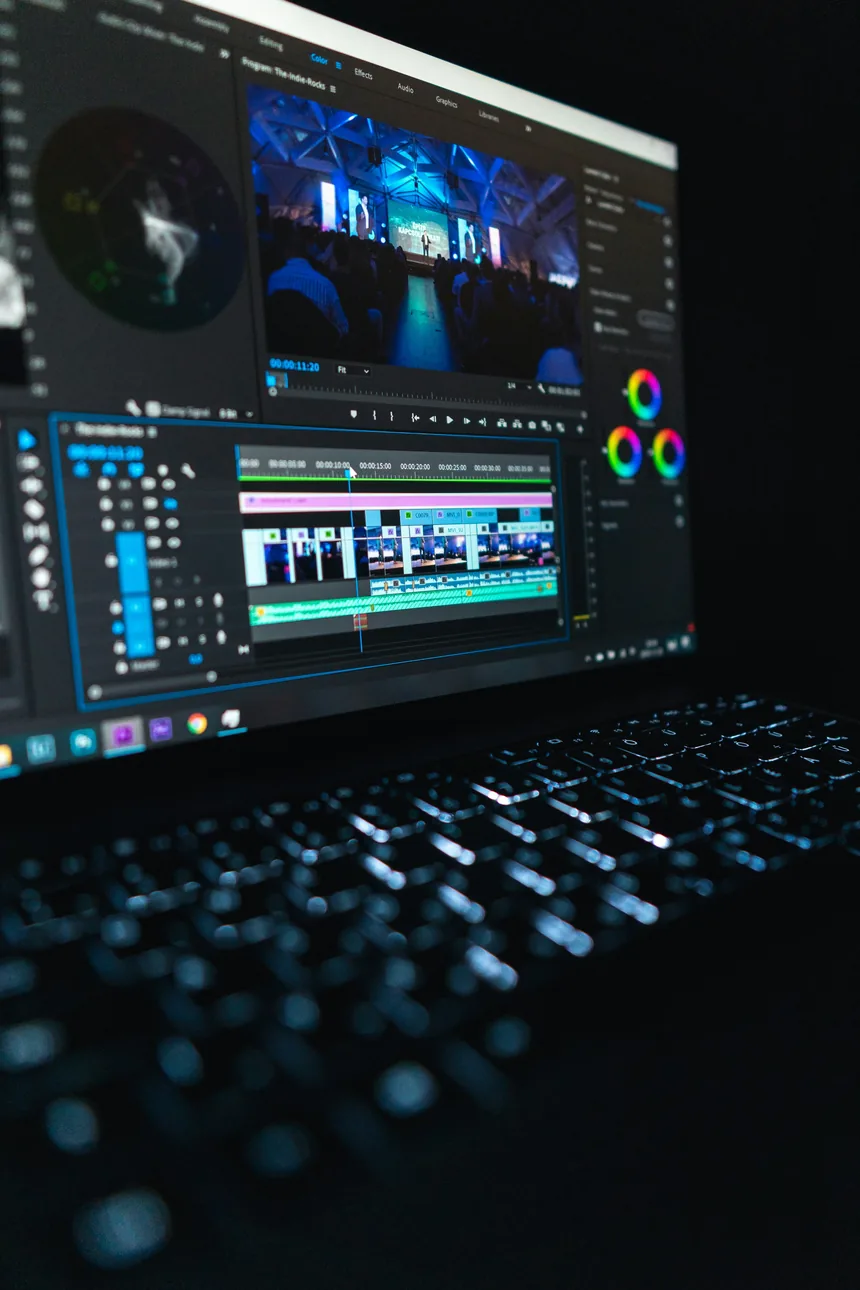 A video editing timeline and colour wheels on a monitor above a backlit keyboard