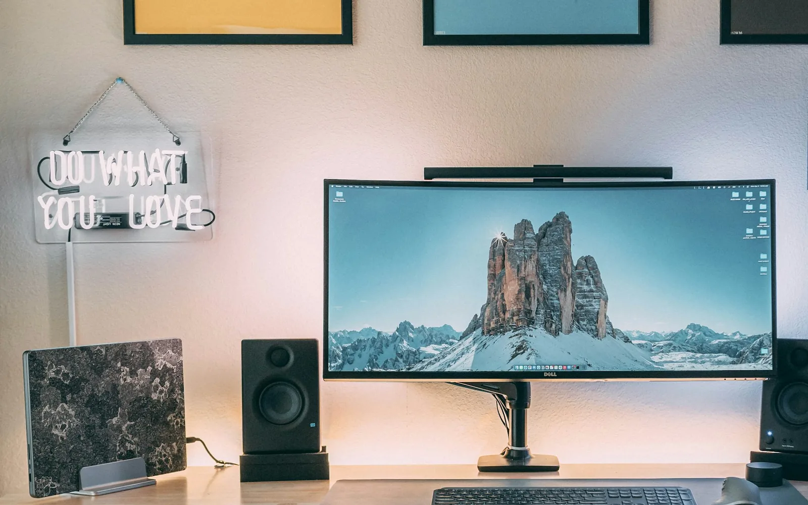 The studio desk: an ultrawide monitor on a wooden desk, framed prints above it and warm light behind the screen