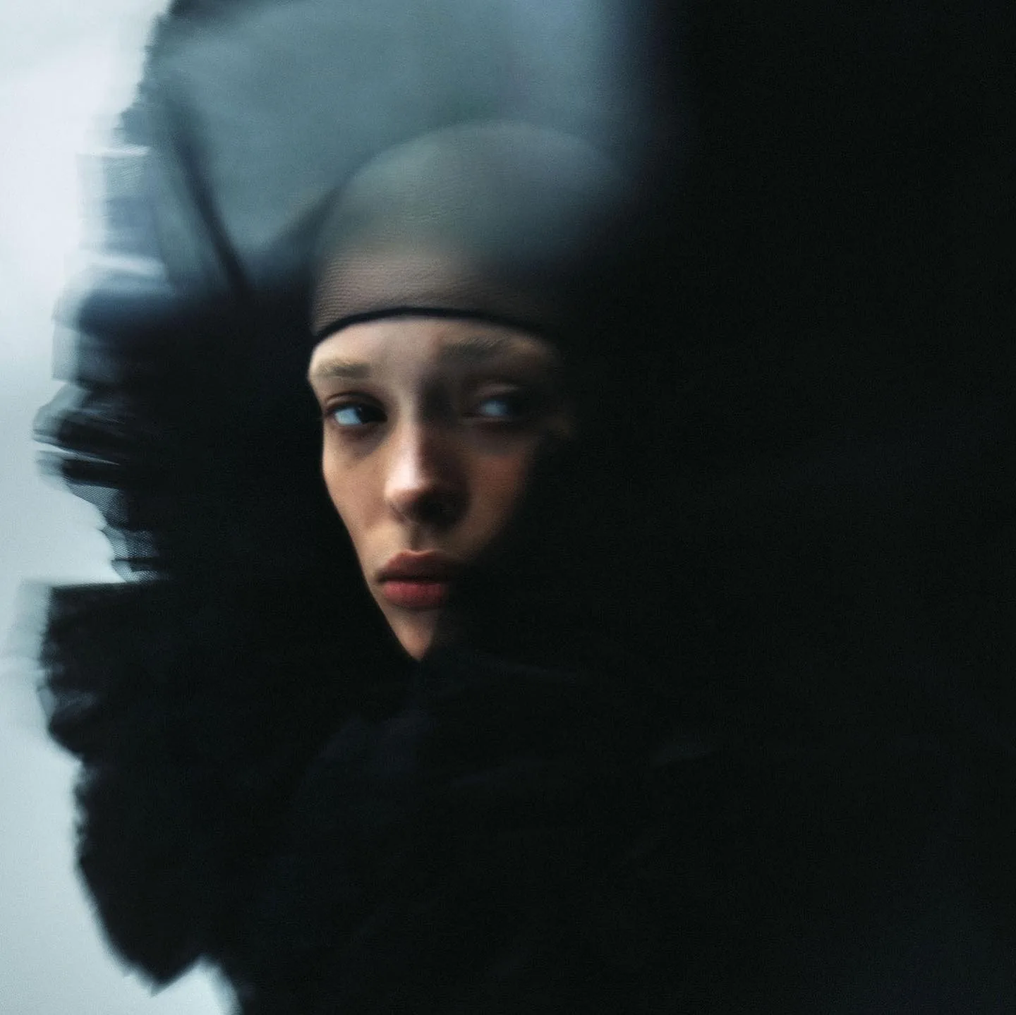 A model in a close-fitting black mesh cap, turned away, with a dark tulle veil sweeping across the frame