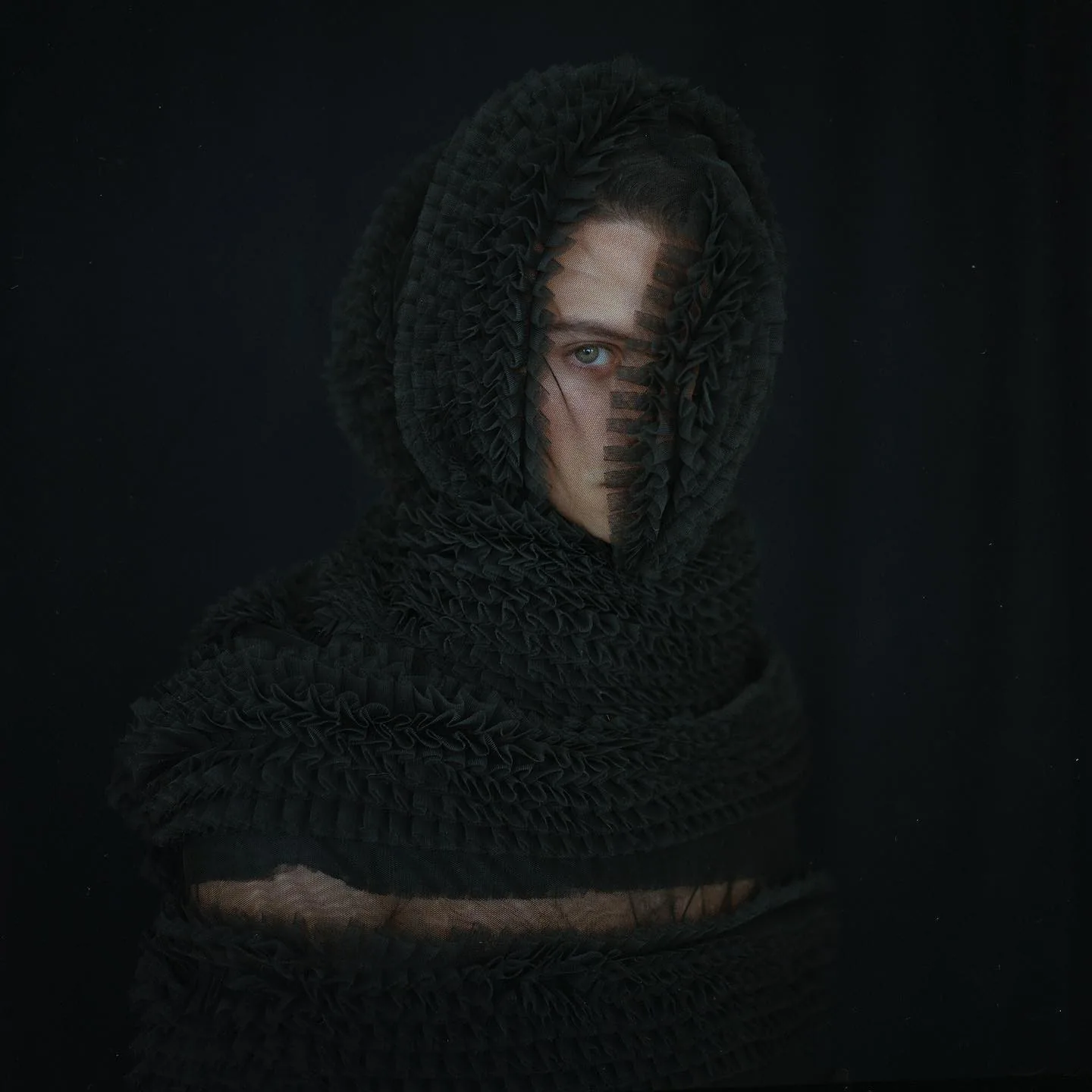 A full-length black tulle hood and wrap, gathered in tight rows, photographed against a black ground